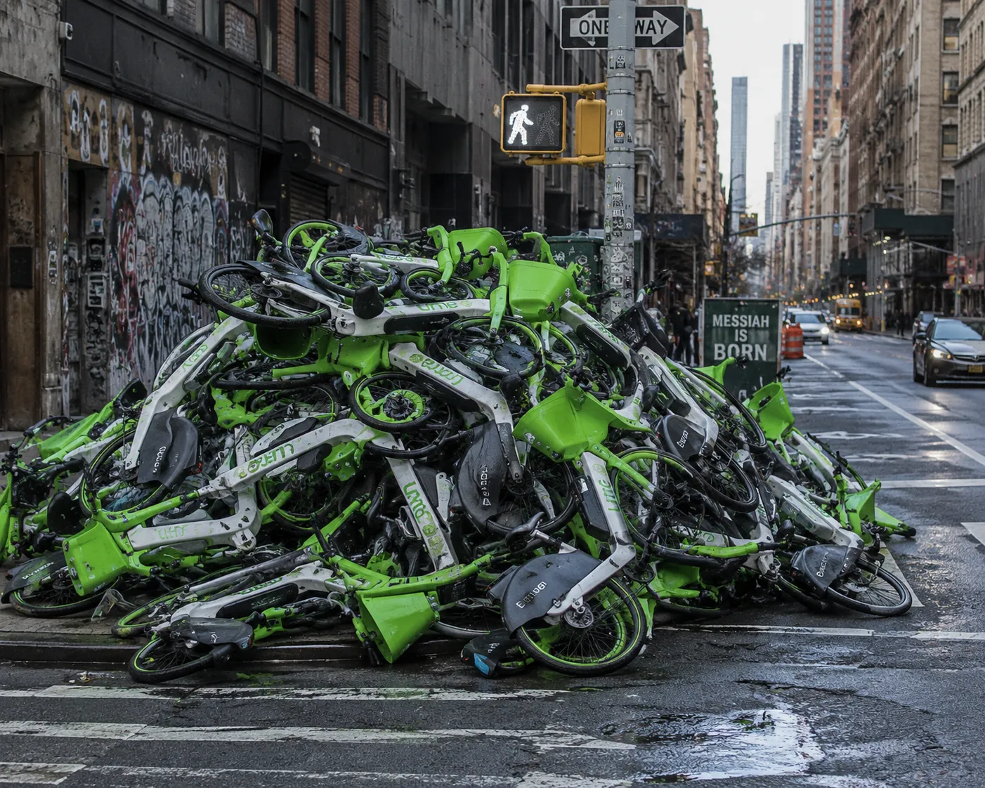A mountain of discarded green-and-white shared e-bikes piled on a city street corner — a trust network with wheels, reduced to scrap; most people see bicycles, not the distributed system underneath.
